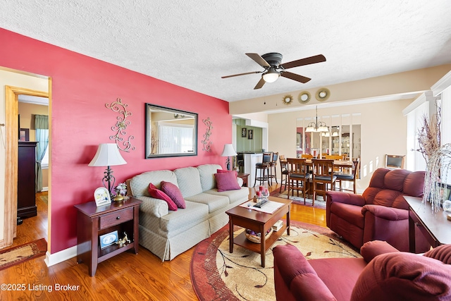 living room with a ceiling fan, a textured ceiling, baseboards, and wood finished floors