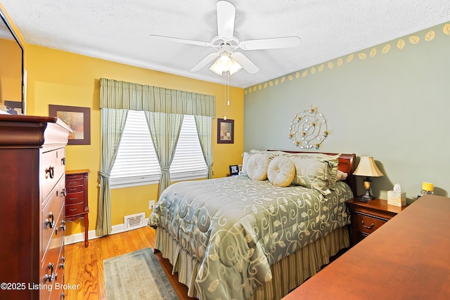 bedroom featuring a textured ceiling, a ceiling fan, baseboards, visible vents, and light wood-style floors