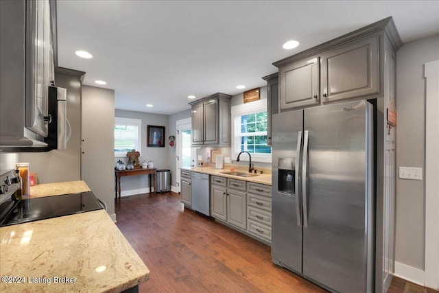 kitchen featuring dark wood finished floors, gray cabinetry, appliances with stainless steel finishes, a sink, and light stone countertops