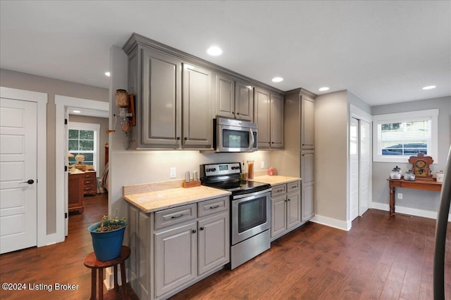 kitchen with baseboards, appliances with stainless steel finishes, dark wood-style flooring, light stone countertops, and gray cabinetry