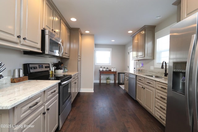 kitchen featuring appliances with stainless steel finishes, light stone countertops, a sink, and dark wood-style floors