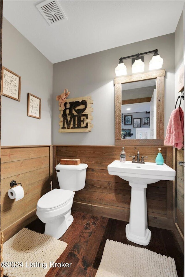 half bath with toilet, a wainscoted wall, wood walls, wood finished floors, and visible vents