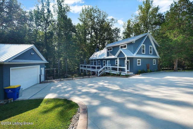 view of front of house featuring driveway, a garage, metal roof, covered porch, and fence