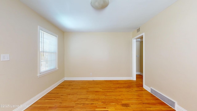 empty room with light wood finished floors, visible vents, and baseboards