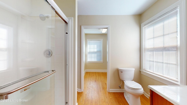 bathroom with toilet, a stall shower, vanity, wood finished floors, and baseboards