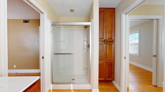 bathroom featuring wood finished floors, vanity, baseboards, visible vents, and a shower stall