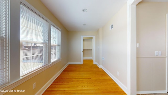 hall with light wood-type flooring, visible vents, and baseboards