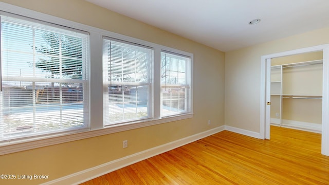 unfurnished bedroom featuring light wood-style floors, a walk in closet, a closet, and baseboards