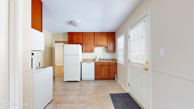 kitchen with white appliances, stacked washer and dryer, brown cabinetry, light countertops, and a sink