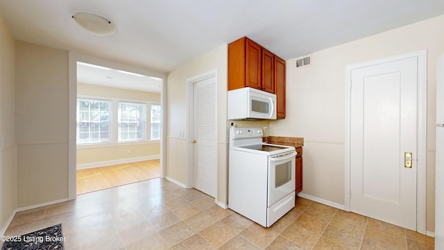 kitchen featuring brown cabinetry, white appliances, visible vents, and baseboards