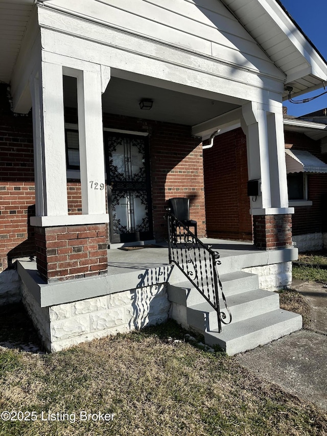 doorway to property featuring covered porch and brick siding