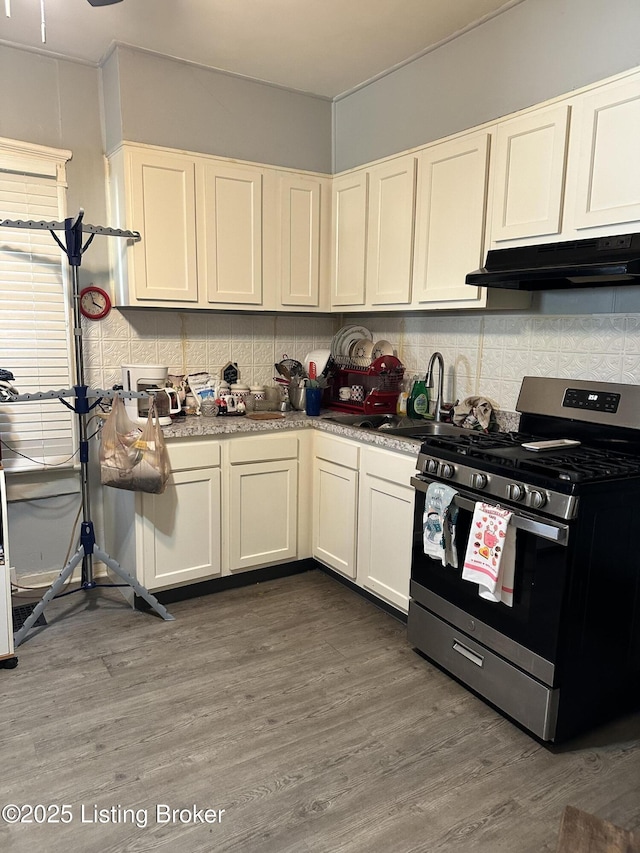 kitchen with under cabinet range hood, stainless steel gas range oven, dark wood-style flooring, and backsplash