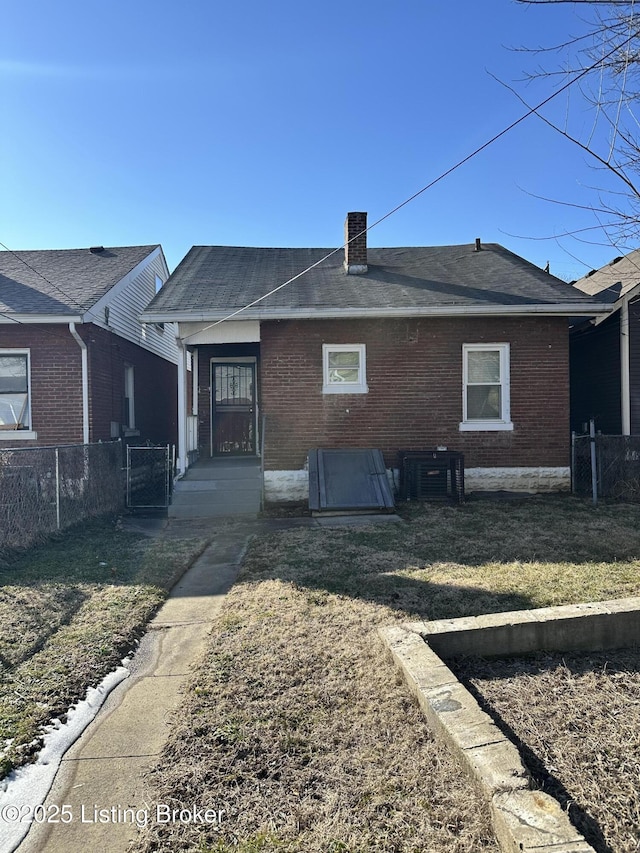 rear view of house with brick siding, a chimney, a lawn, central AC, and fence