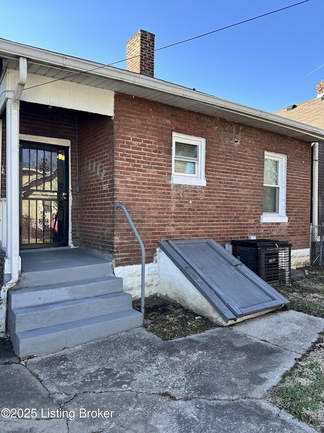 view of exterior entry featuring central AC, brick siding, and a chimney