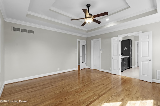 unfurnished bedroom featuring a tray ceiling, crown molding, visible vents, light wood-type flooring, and baseboards