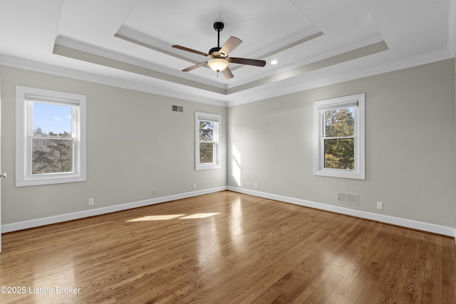 empty room with baseboards, visible vents, a tray ceiling, and wood finished floors