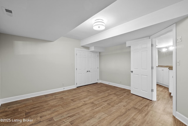 finished below grade area with light wood-type flooring, visible vents, and baseboards