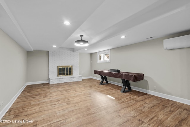 interior space with a brick fireplace, an AC wall unit, baseboards, and wood finished floors