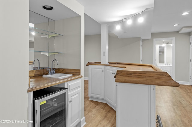 bar featuring light wood finished floors, baseboards, wine cooler, a sink, and track lighting