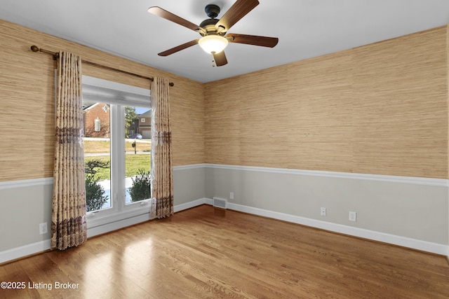 empty room featuring a ceiling fan, wood finished floors, visible vents, and baseboards