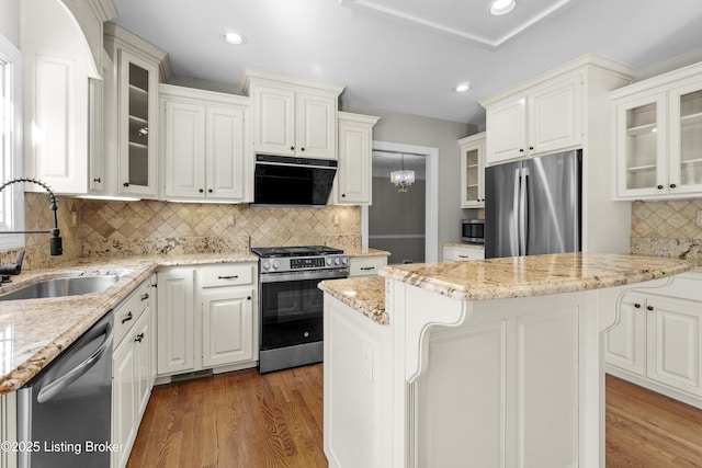 kitchen featuring light stone counters, stainless steel appliances, a sink, wood finished floors, and exhaust hood