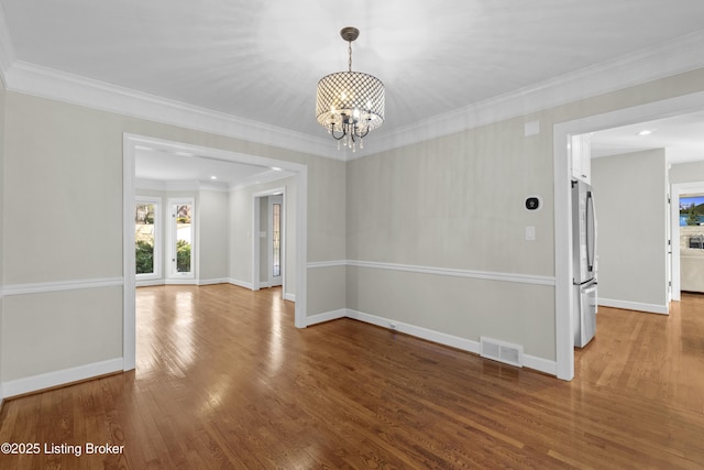 empty room featuring baseboards, wood finished floors, visible vents, and an inviting chandelier