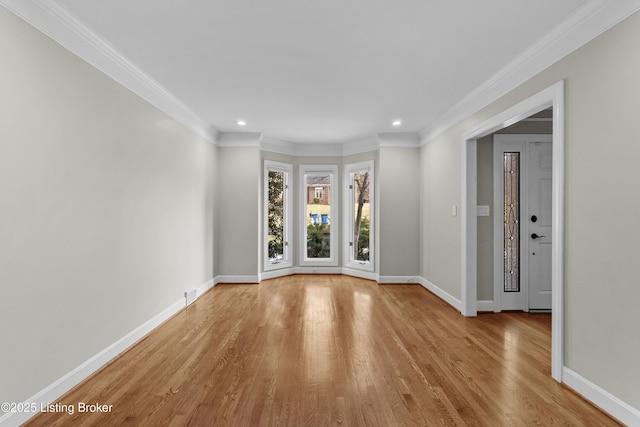 empty room featuring light wood finished floors, baseboards, and crown molding