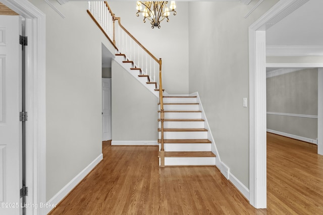 staircase with ornamental molding, a notable chandelier, baseboards, and wood finished floors