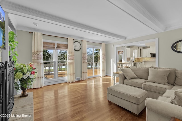 living room featuring light wood-style flooring, visible vents, ornamental molding, and beamed ceiling