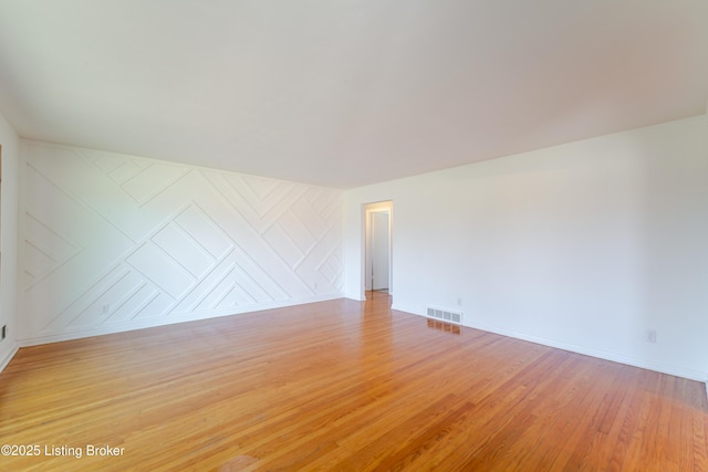 unfurnished room with an accent wall, light wood-type flooring, visible vents, and baseboards