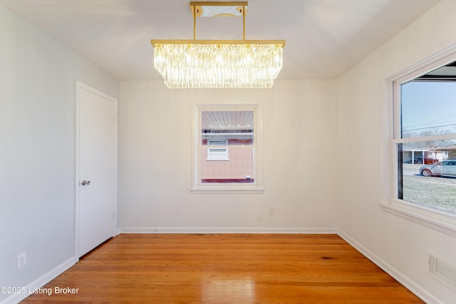 unfurnished room featuring visible vents, light wood-style flooring, baseboards, and an inviting chandelier