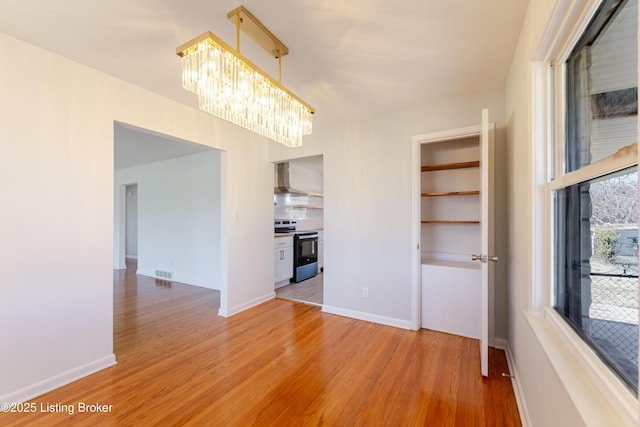 unfurnished dining area with light wood-style floors, baseboards, visible vents, and a notable chandelier