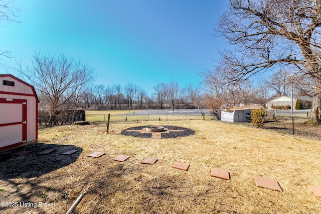 view of yard featuring a fire pit, a storage unit, fence, and an outbuilding