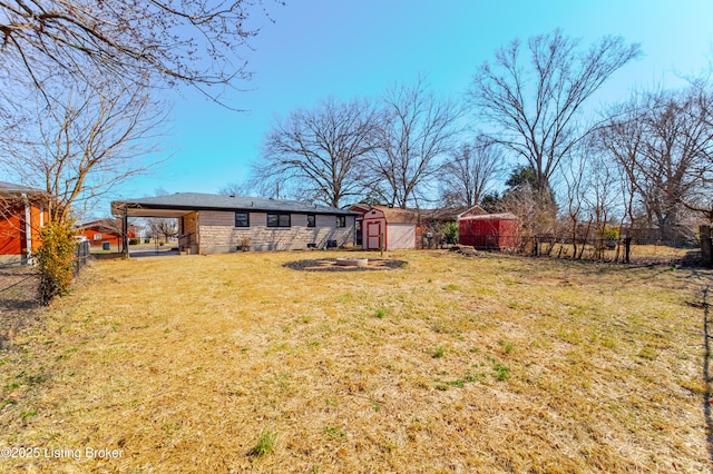 view of yard featuring a fire pit, fence, and an outdoor structure