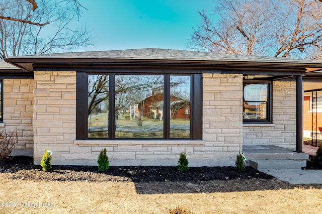 view of home's exterior with stone siding and a shingled roof