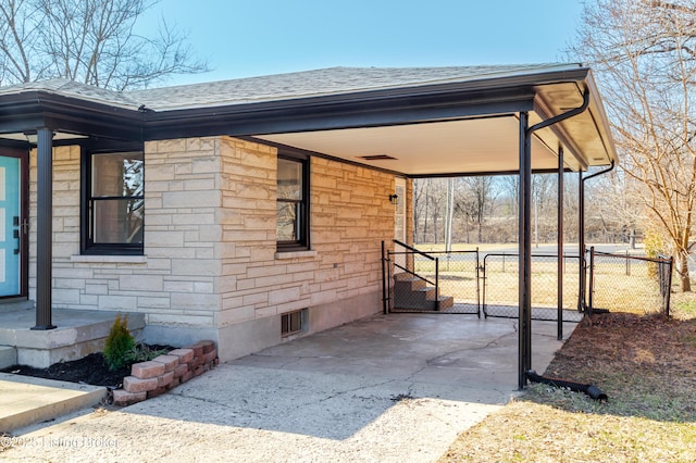 exterior space featuring roof with shingles, concrete driveway, a gate, fence, and stone siding