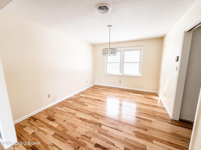 unfurnished dining area featuring a textured ceiling, wood finished floors, visible vents, and baseboards