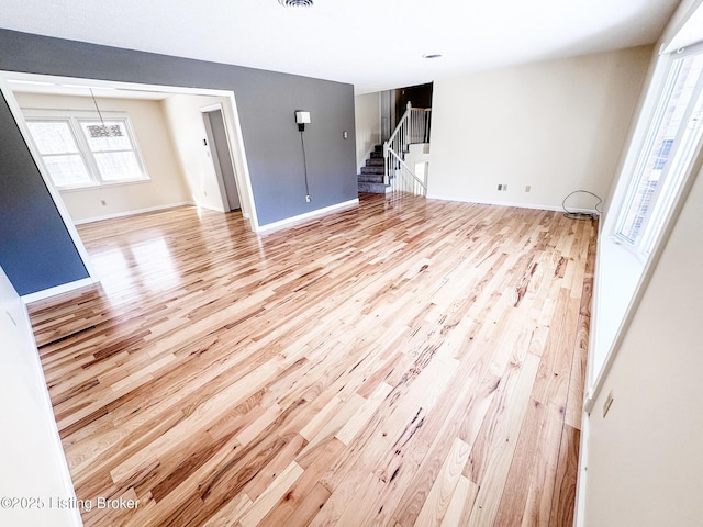 unfurnished living room with stairway, light wood-style flooring, and baseboards