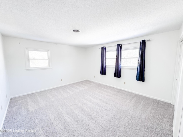 carpeted empty room featuring a healthy amount of sunlight, visible vents, and a textured ceiling