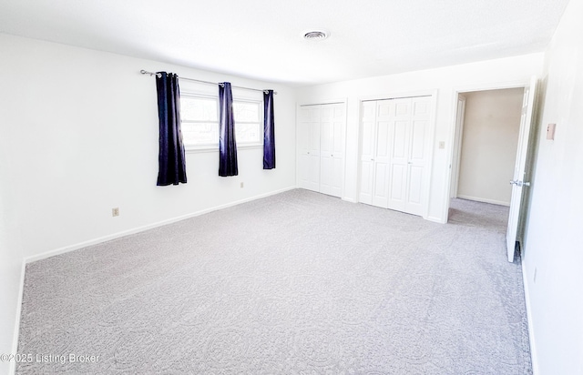 unfurnished bedroom with light carpet, baseboards, visible vents, and multiple closets