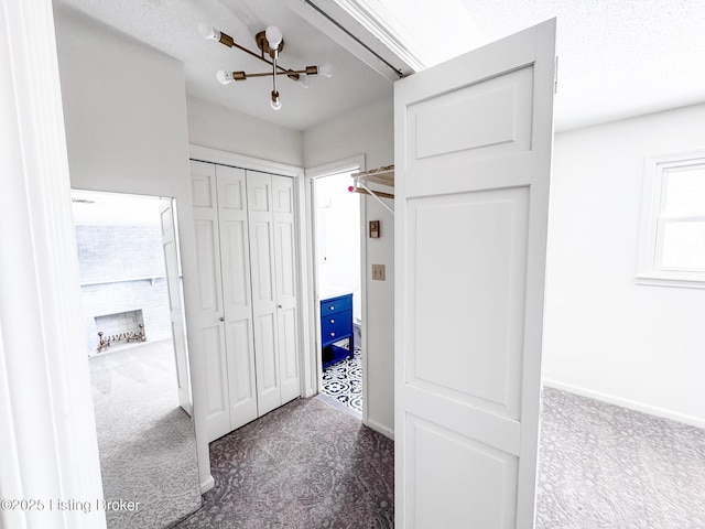 hallway featuring dark carpet, a textured ceiling, and baseboards