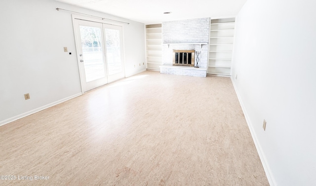 unfurnished living room with a brick fireplace, baseboards, light wood-style floors, and built in features