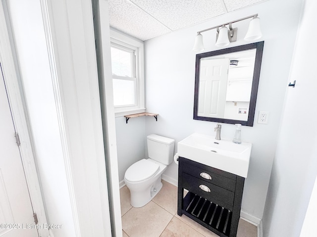 bathroom with toilet, vanity, tile patterned flooring, a drop ceiling, and baseboards