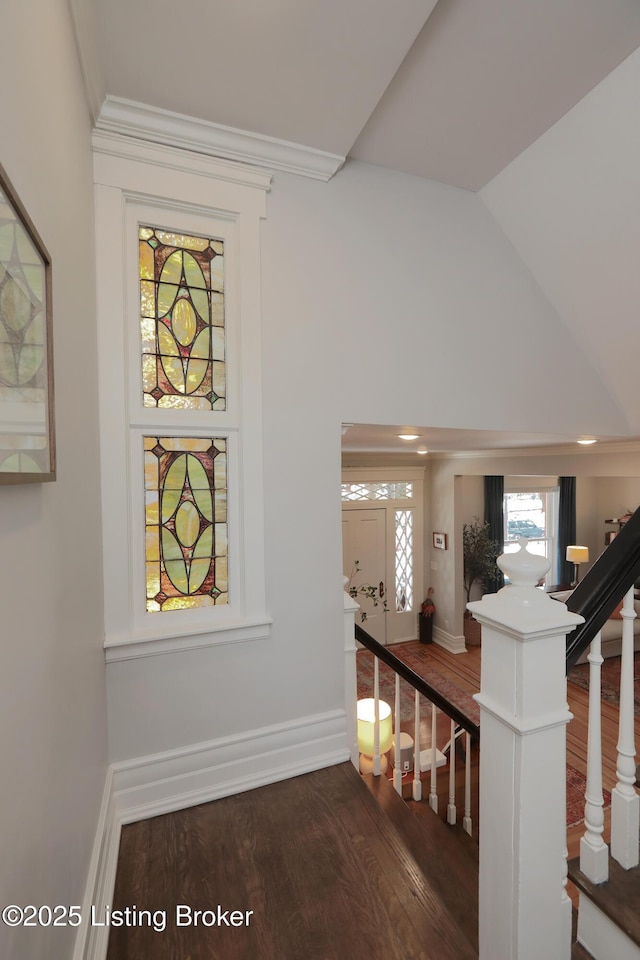 hall featuring lofted ceiling, wood finished floors, baseboards, stairs, and ornamental molding