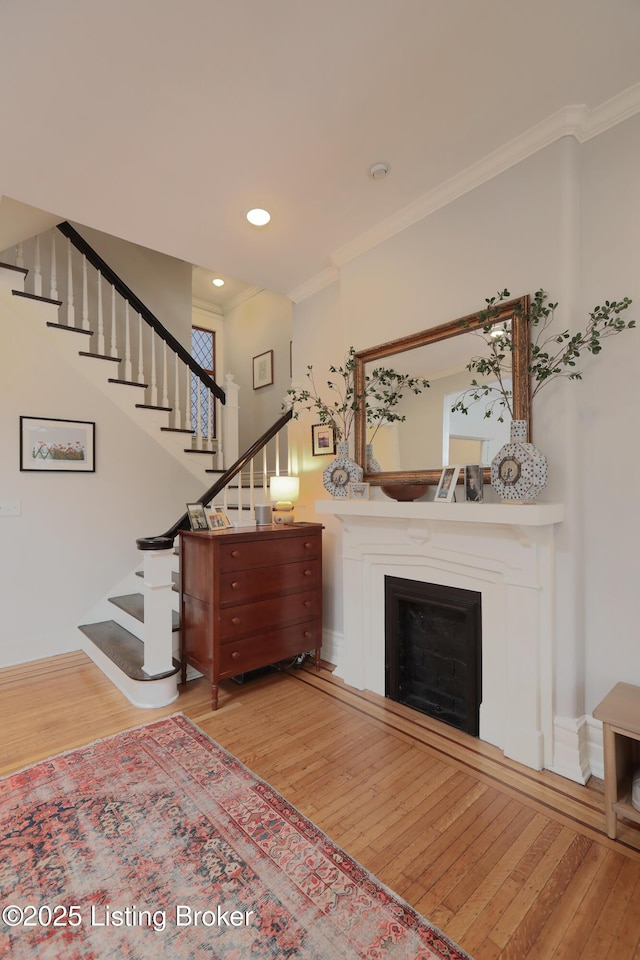 unfurnished living room with recessed lighting, a fireplace, wood finished floors, ornamental molding, and stairway