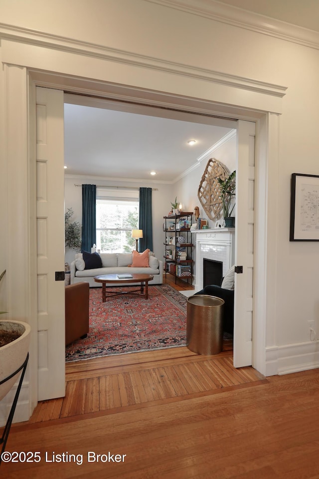 living area with baseboards, a fireplace, ornamental molding, and wood finished floors