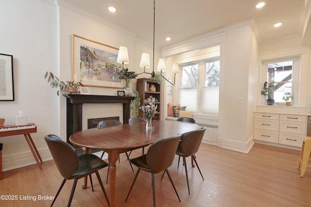 dining room with light wood-type flooring, a brick fireplace, baseboards, and ornamental molding