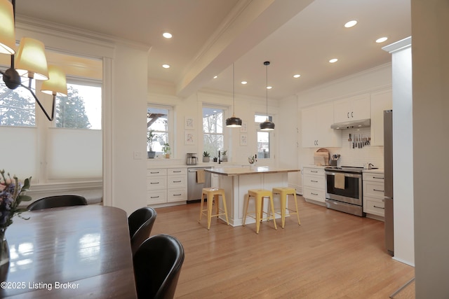 kitchen with a breakfast bar, a kitchen island, white cabinetry, light countertops, and appliances with stainless steel finishes