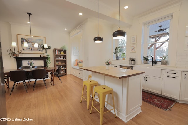 kitchen with a center island, a breakfast bar area, hanging light fixtures, white cabinets, and wood counters