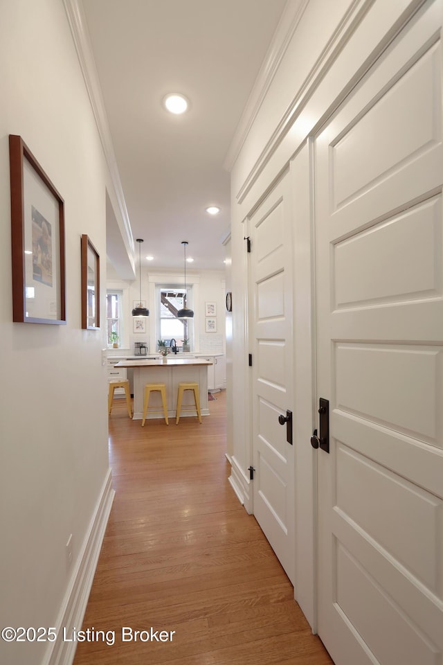 corridor with light wood finished floors, ornamental molding, baseboards, and recessed lighting